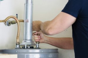 Adult male making adjustments and tightening connection on new hot water heater - V-Max Plumbing