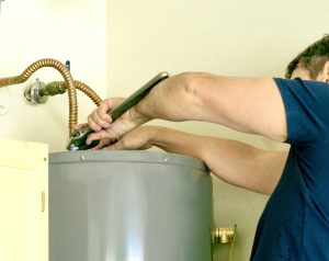 Adult male using a wrench to make adjustments on top of a hot water heater - V-Max Plumbing