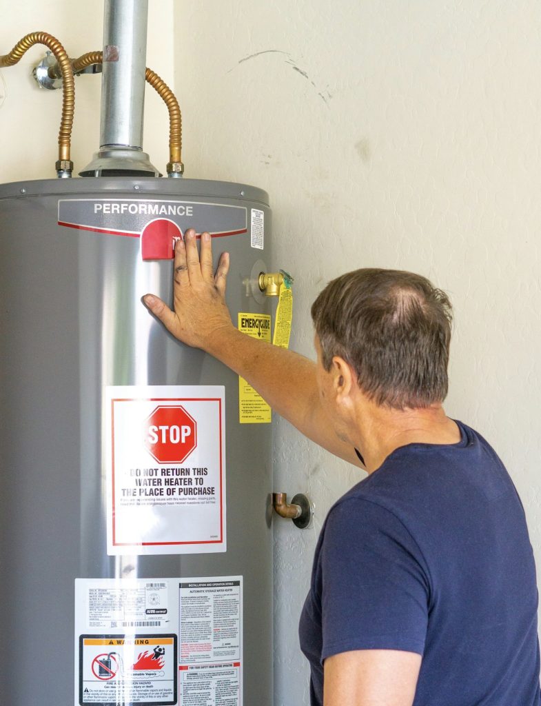 Adult male with hand on newly installed hot water heater - V-Max Plumbing