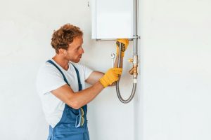 Repairing water heater. Young man working in uniform at construction at daytime - V-Max Plumbing