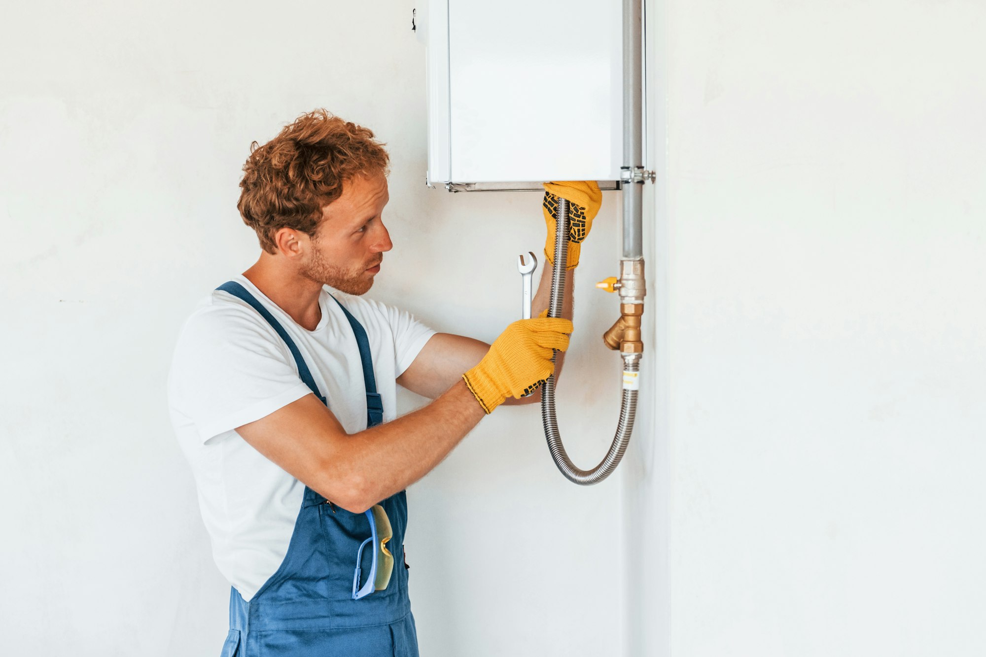 Repairing water heater. Young man working in uniform at construction at daytime